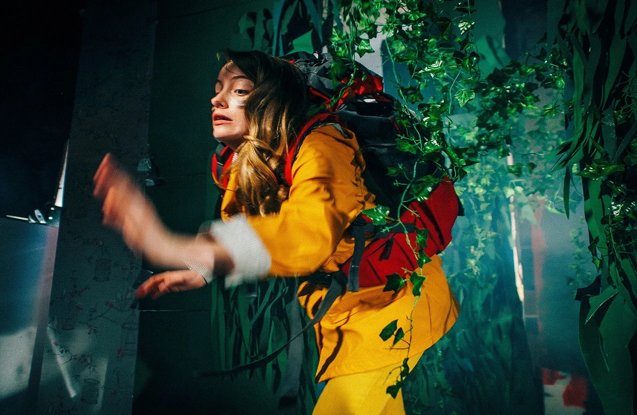 Vagaband film still: a woman in a yellow jacket surrounded by plants on a film set